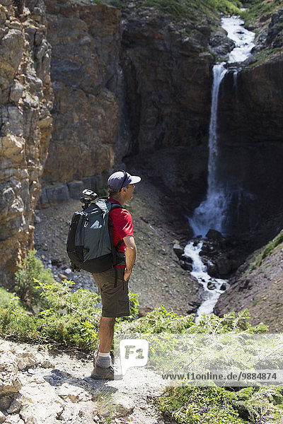 A male hiker overlooking a waterfall on a trail; Waterton  Alberta  Canada