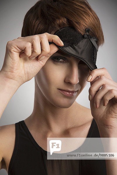 Studio-Porträt einer Frau  die aus einer schwarzen Augenmaske schaut.