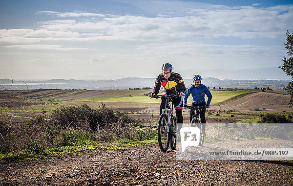 Two male mountain bikers cycling up dirt track  Cagliari  Sardinia  Italy