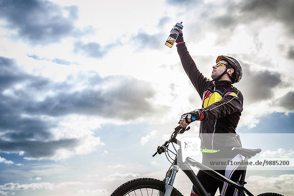 Mittlerer Erwachsener männlicher Mountainbiker feiert mit Wasserflasche