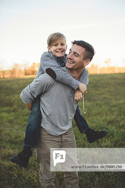 Boy getting piggy back from father in field