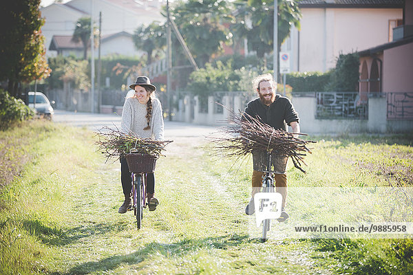 Young couple carrying bunches of sticks on bicycles