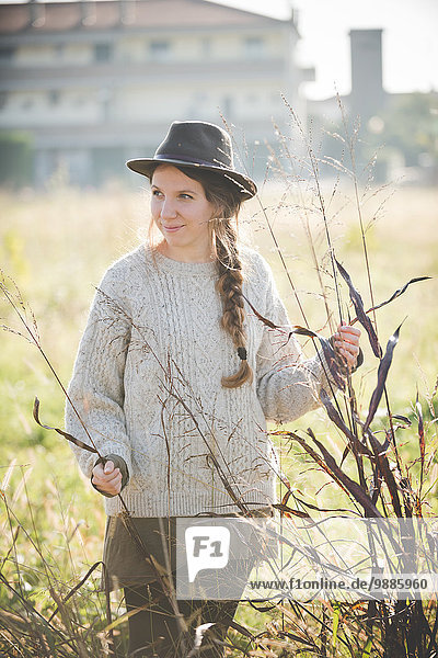 Young woman wearing hat touching plants in field