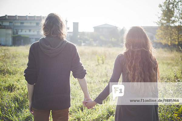 Young couple holding hands in field in sunlight