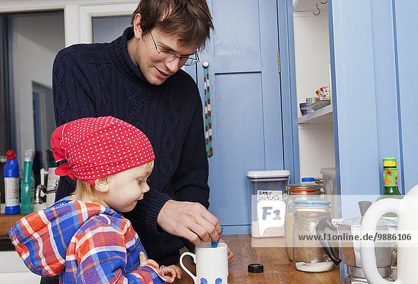 Father making cup of tea with son in kitchen