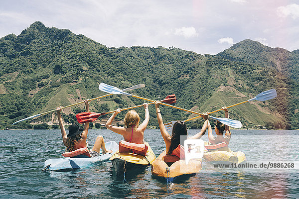 Rear view of four female friends celebrating in kayaks on Lake Atitlan  Guatemala