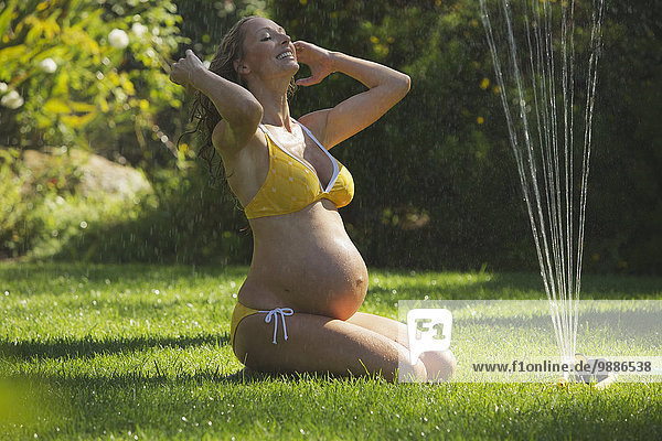 Frau sitzend Bikini nass Rasen Rasensprenger Schwangerschaft Verbindung