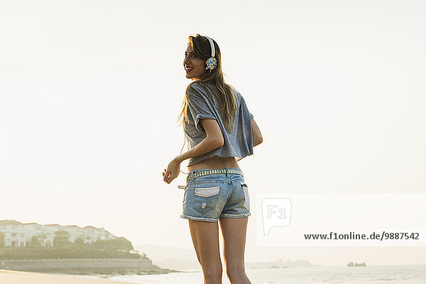 Young woman listening to music with her headphones on the beach; Xiamen  China