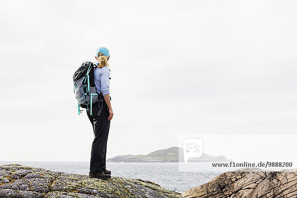 Female hiker on rounded rocks overlooks ocean and island in the distance; Omey Island  County Galway  Ireland