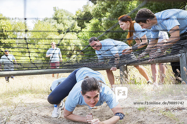 Determined woman crawling under net on boot camp obstacle course