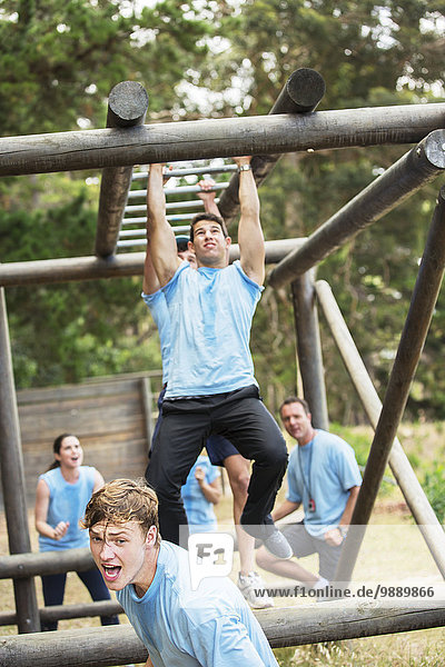 Determined man crossing monkey bars on boot camp obstacle course