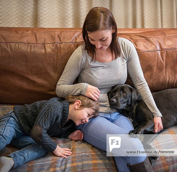 Mother and son relaxing on sofa at home with pet labrador