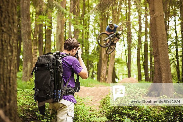 Young male photographer photographing mountain biker in forest