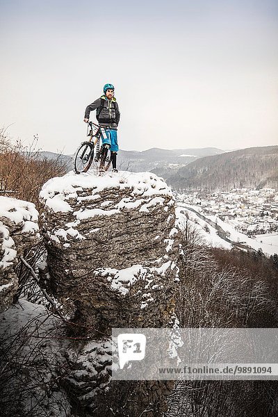 Young male mountain biker on top of snow covered rock formation