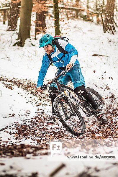 Junge männliche Mountainbiker  die auf verschneiten Waldwegen rasen