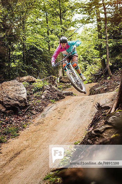 Young female mountain biker jumping mid air in forest