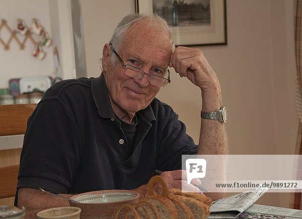Porträt eines älteren Mannes  sitzend am Frühstückstisch mit Zeitung