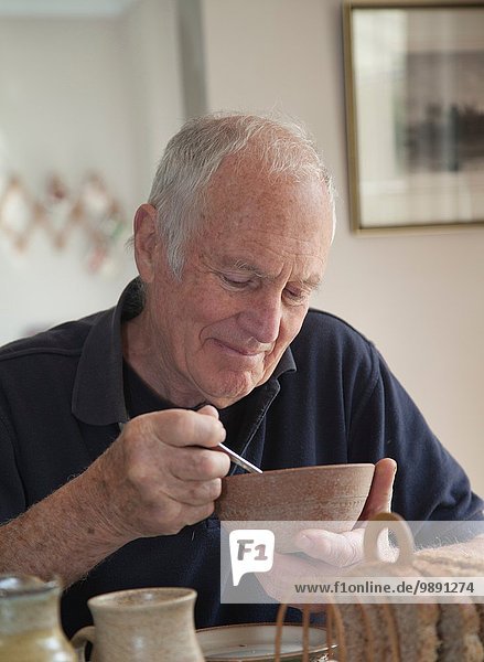 Älterer Mann  sitzt am Tisch  isst eine Schüssel mit Müsli.