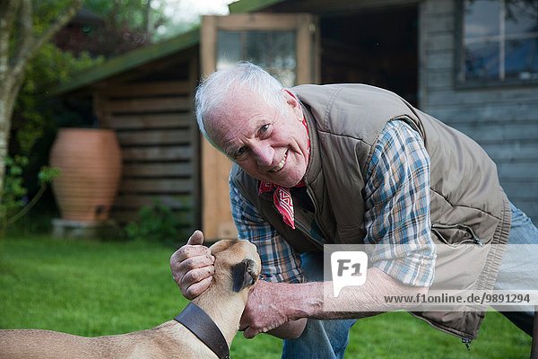 Senior Mann  streichelnder Hund im Garten