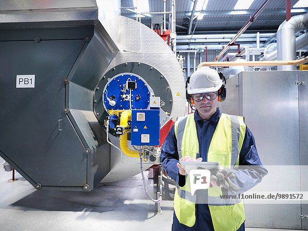 Arbeiter überprüft Messwerte auf digitalen Tabletten in einem Gaskraftwerk