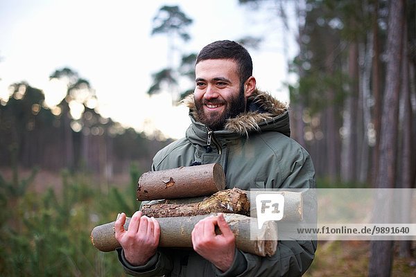 Young man collecting logs for campfire in forest