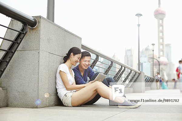 Touristenpaar auf der Brücke sitzend mit Blick auf digitales Tablett  The Bund  Shanghai  China