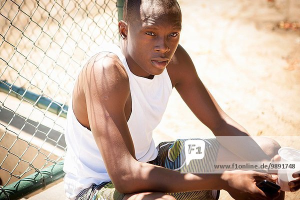 Portrait of young male basketball player with smartphone and drinking water