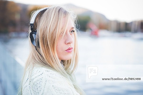 Junge Frau schaut weg und hört Kopfhörer am Seeufer  Como  Italien