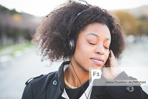 Nahaufnahme einer jungen Frau  die Kopfhörer mit geschlossenen Augen am Comer See hört.