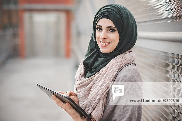 Portrait of young woman wearing hijab using digital tablet on footbridge