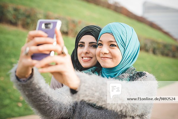 Two female friends in park taking smartphone selfie