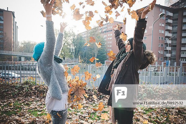Zwei junge Frauen werfen Herbstlaub in den Park.
