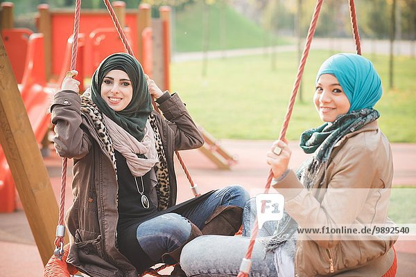 Portrait of two young women sitting on playground swings