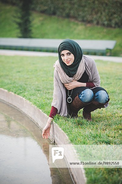 Porträt einer jungen Frau  die Hijab trägt und am Parksee hockt