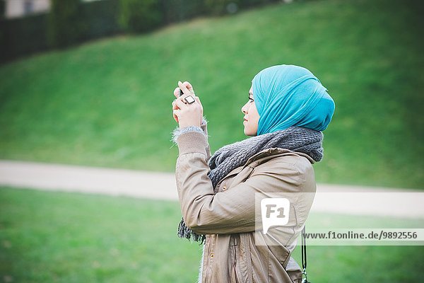 Junge Frau im Park fotografiert mit Smartphone