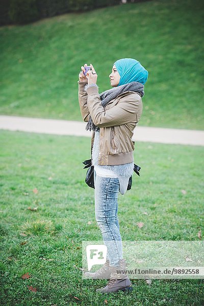 Junge Frau im Park fotografiert auf dem Smartphone