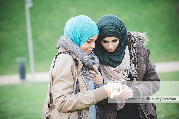 Two female friends in park reading text on smartphones