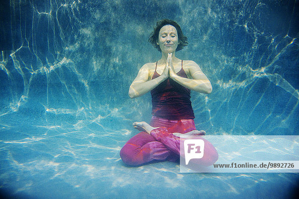 Reife Frau in roter Yogahose und Weste  in Yogastellung  Unterwassersicht