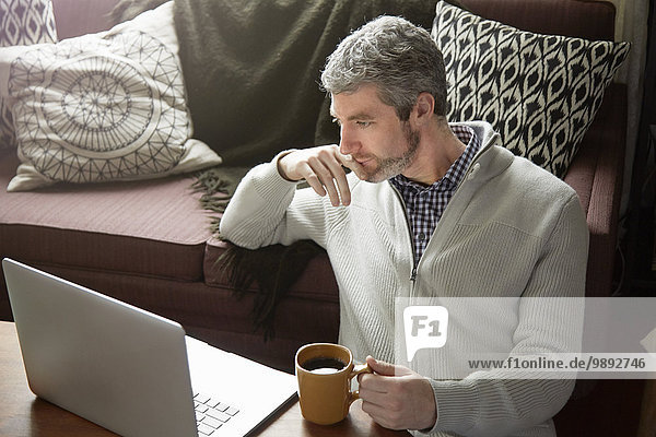 Junger Mann trinkt Kaffee und surft auf dem Laptop