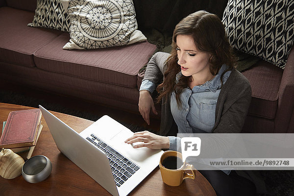 Junge Frau trinkt Kaffee und surft auf dem Laptop