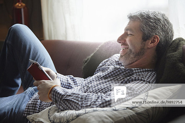 Young man reclining on living room sofa using digital tablet