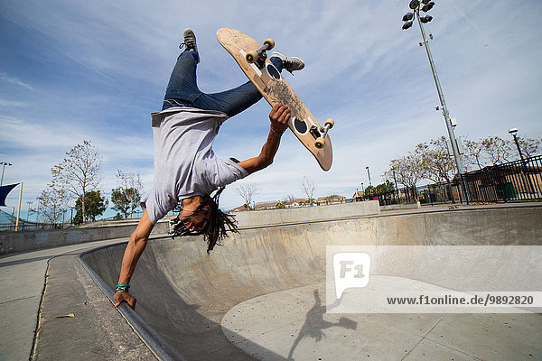 Young man doing skateboard trick upside down on edge of skateboard park