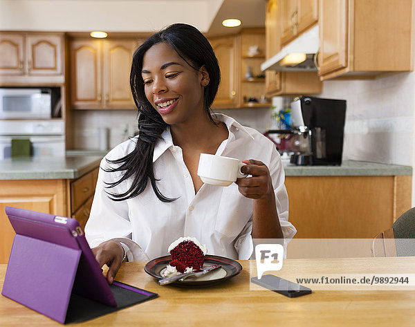 Junge Frau mit digitalem Tablett am Küchentisch