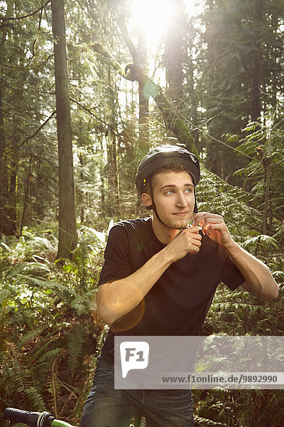 Junger Mann auf dem Fahrrad im Wald  Fahrradhelm sichern