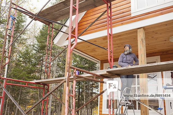 Mid adult woman standing on scaffolding stepladder outside house