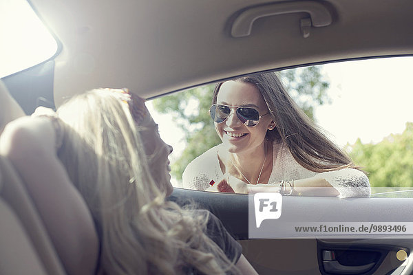 Junge Frau die durch das Autofenster zu ihrem Freund geht.