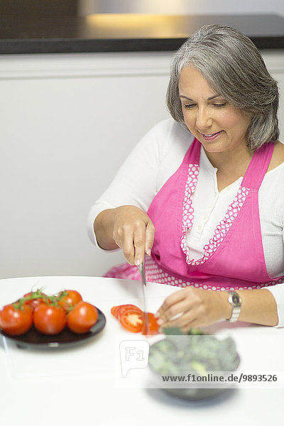 Mature woman slicing tomatoes at table