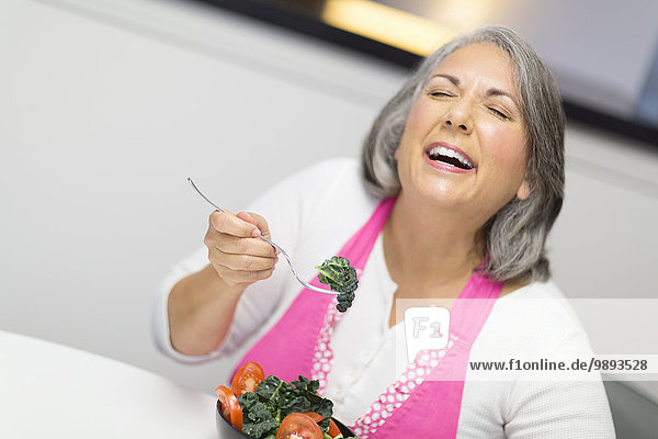 Reife Frau isst Schüssel mit Tomaten und Grünkohl