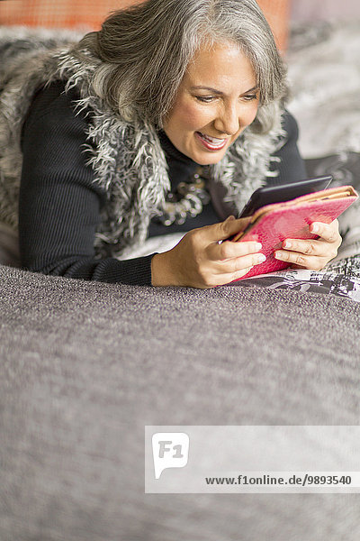 Mature woman relaxing on bed  reading electronic book
