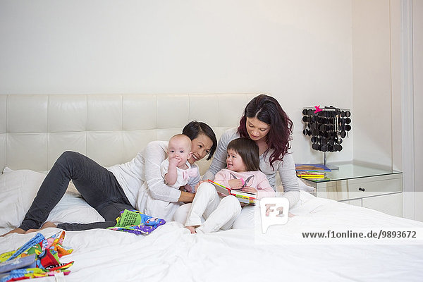Female mid adult couple playing on bed with baby and toddler daughters